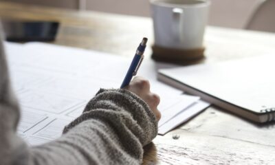 person writing on brown wooden table near white ceramic mug